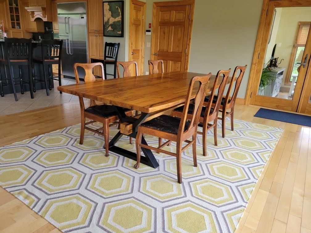 A dining room table with chairs and a rug on the floor.