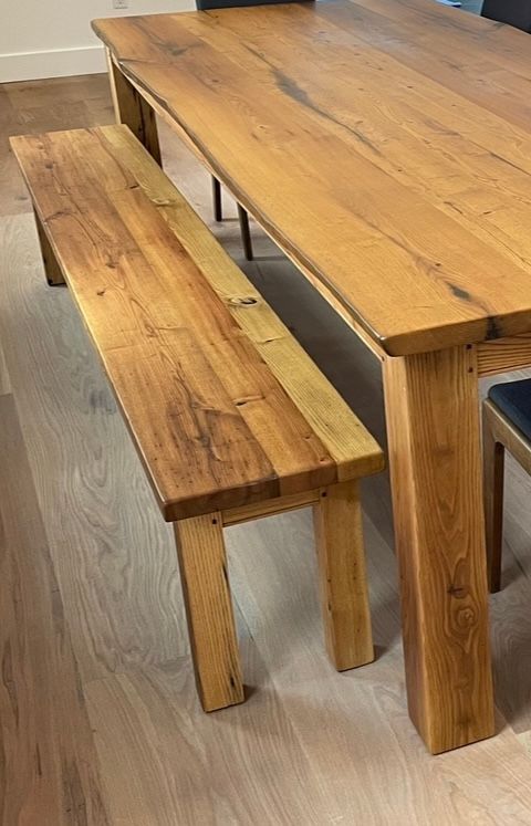 A wooden bench is sitting next to a wooden table.