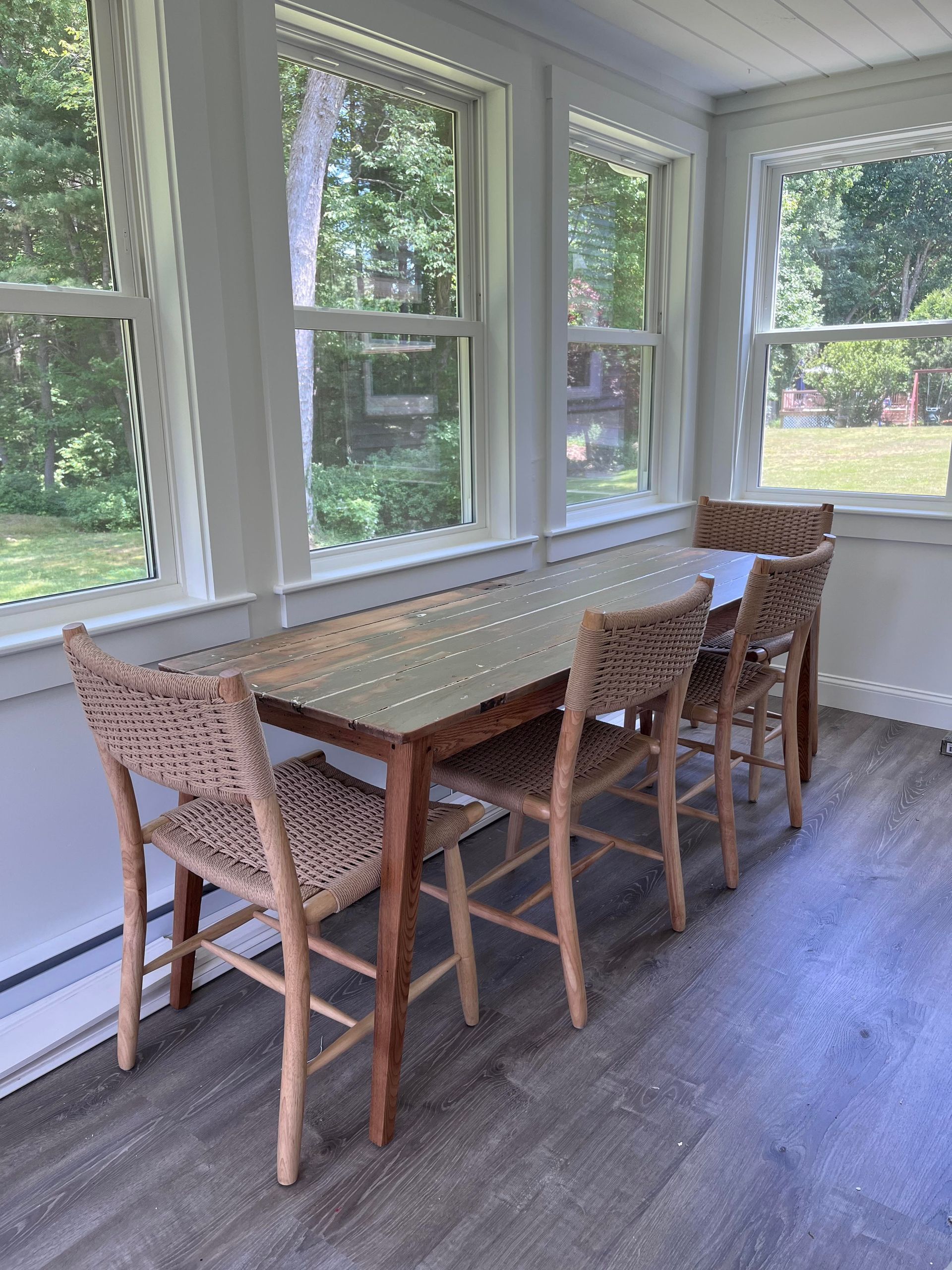 There is a table and chairs in the room with lots of windows.