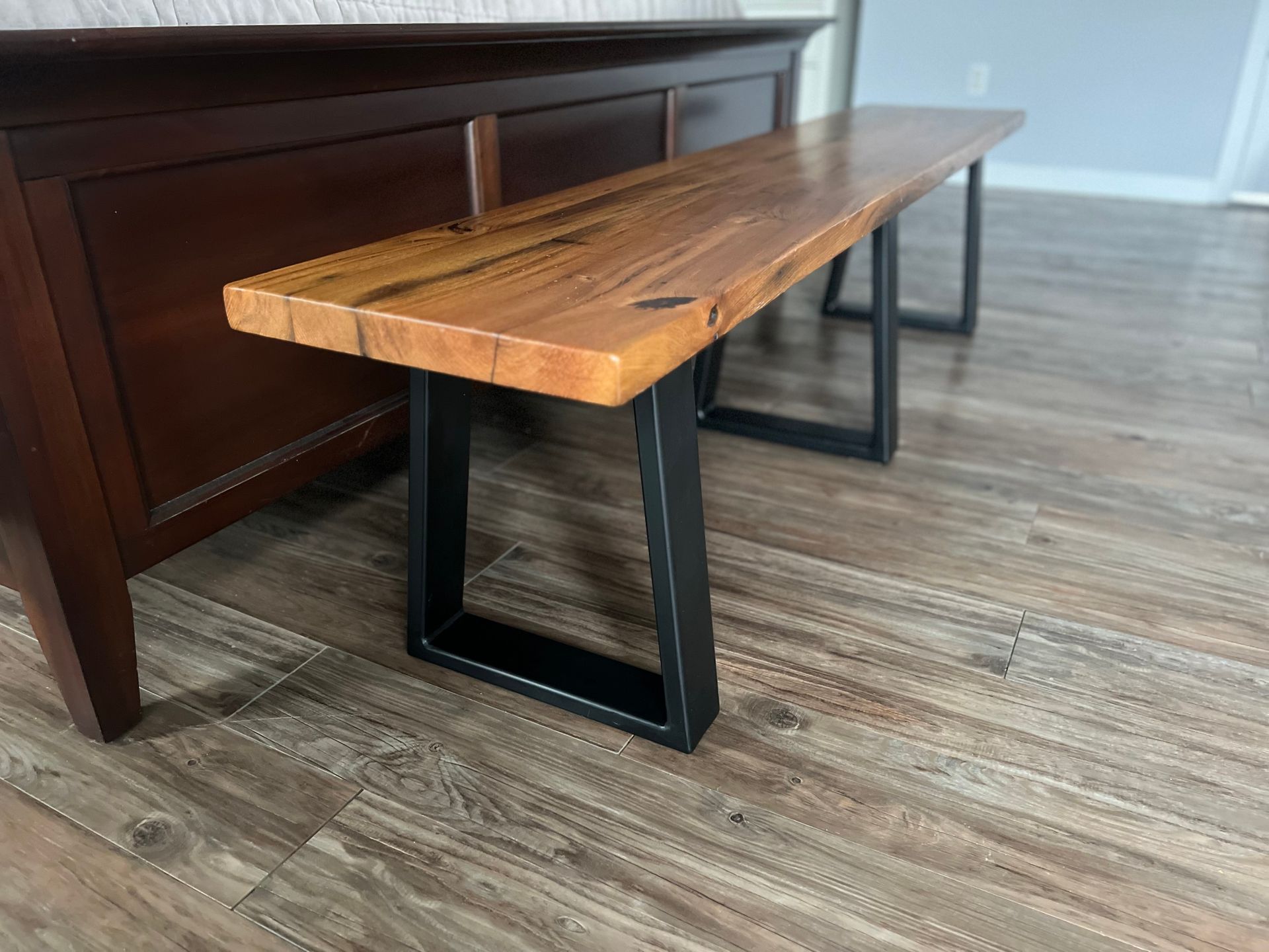 A wooden bench with metal legs is sitting on a wooden floor in a living room.