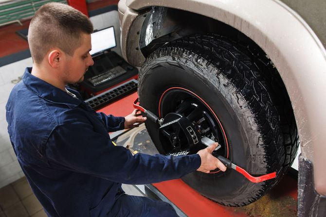 Mechanic in blue jumpsuit using alignment tool on a car tire in a garage.