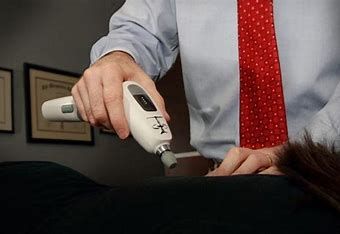 A man in a blue shirt and red tie is using a device on a woman 's back.