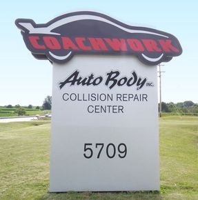 Sign for Coachwork Auto Body, a collision repair center, with address 5709 in a grassy field.