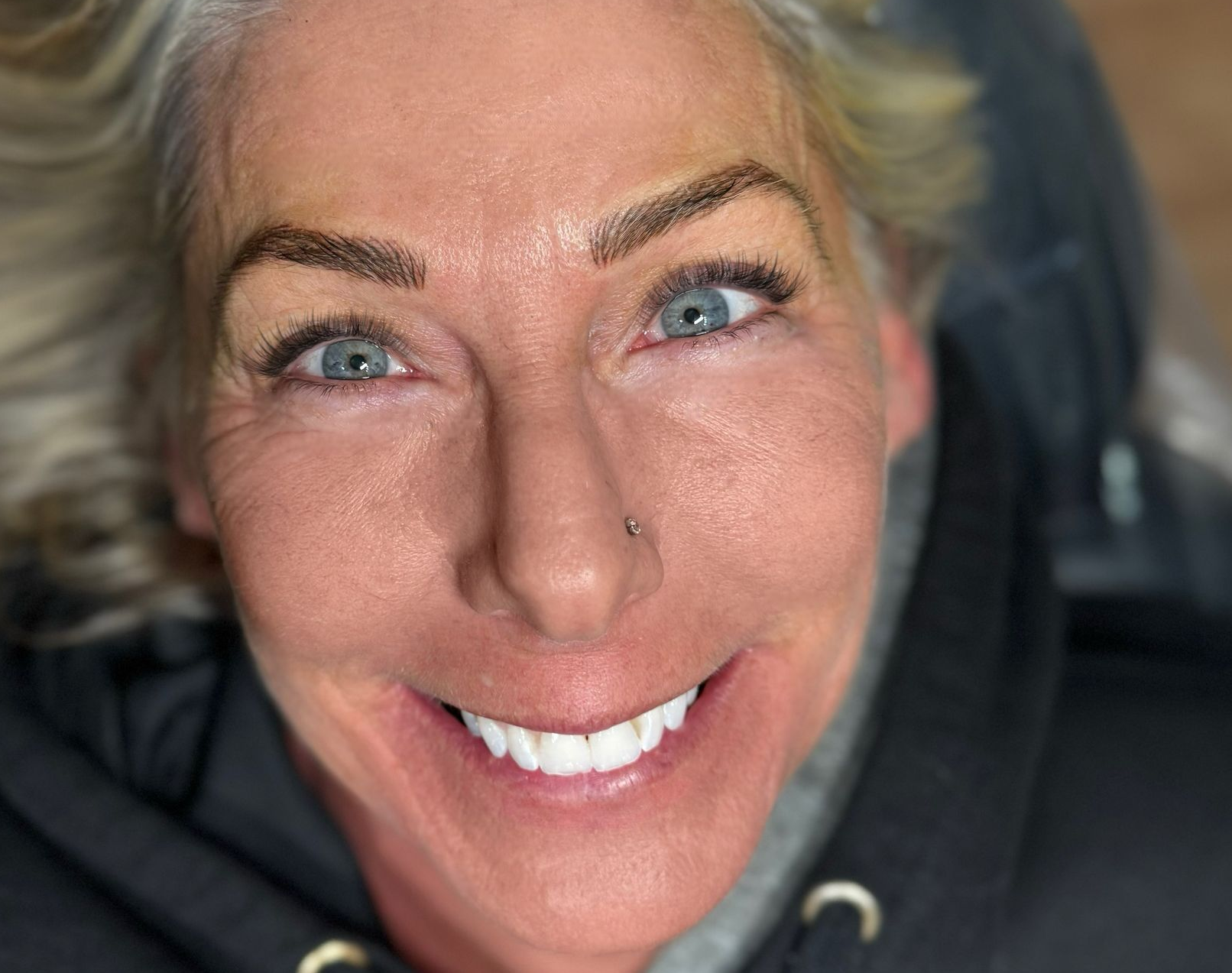 Woman smiling with white teeth, blonde hair, dark hoodie.