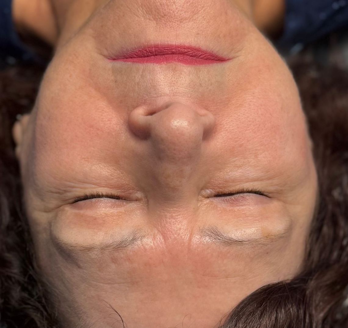 Woman with closed eyes, lying down. Wearing dark top and red lipstick.
