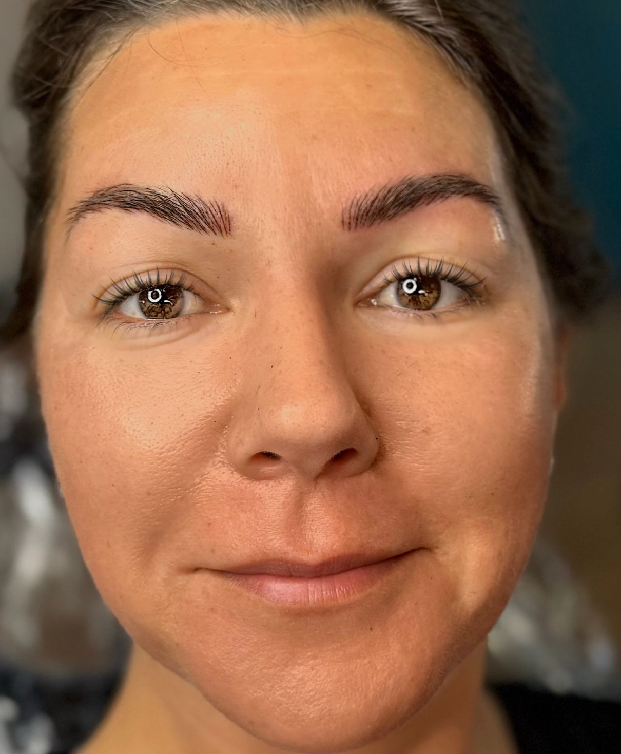 Woman with new eyebrow tattoos, brown skin, smiling, neutral expression.