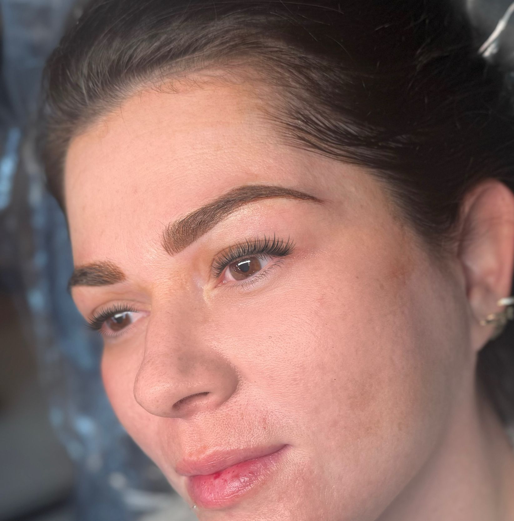 Woman with cosmetic eyebrow tattoos, looking down and to the left. Brown eyebrows, fair skin, light lipstick.