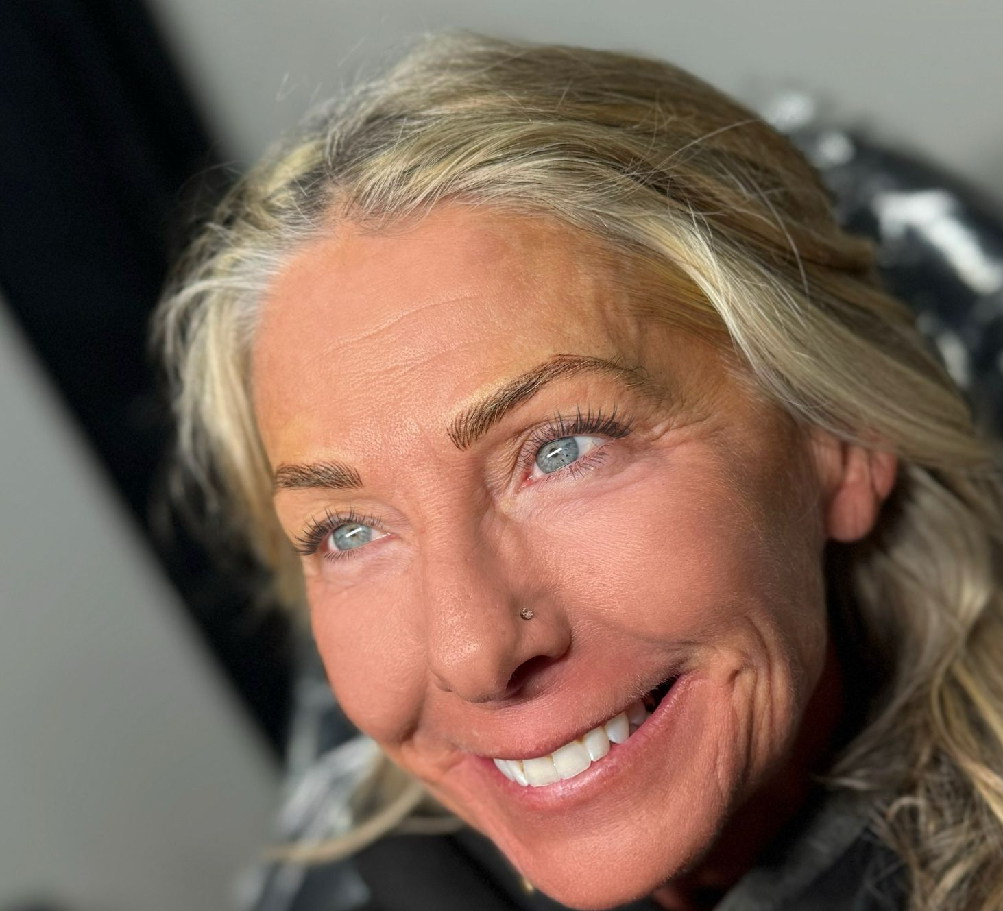 Woman smiling, wearing black hoodie with pink ribbon, blonde hair, blue eyes.