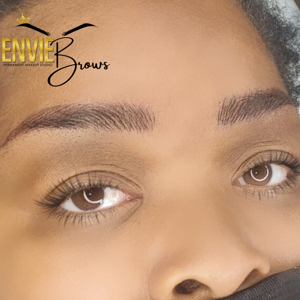 Close-up of a person's eyes and brows, showcasing brow microblading. The brows are shaped and tinted.
