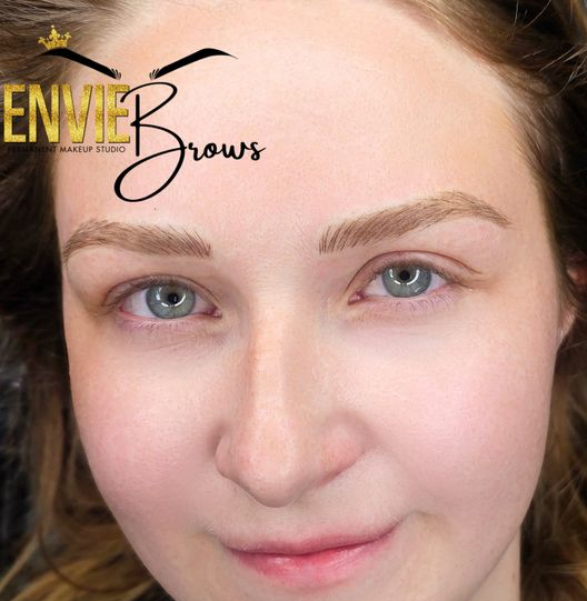 Woman with light brown eyebrows, looking at the camera. She has blue eyes, a slight smile, and is in a beauty studio.
