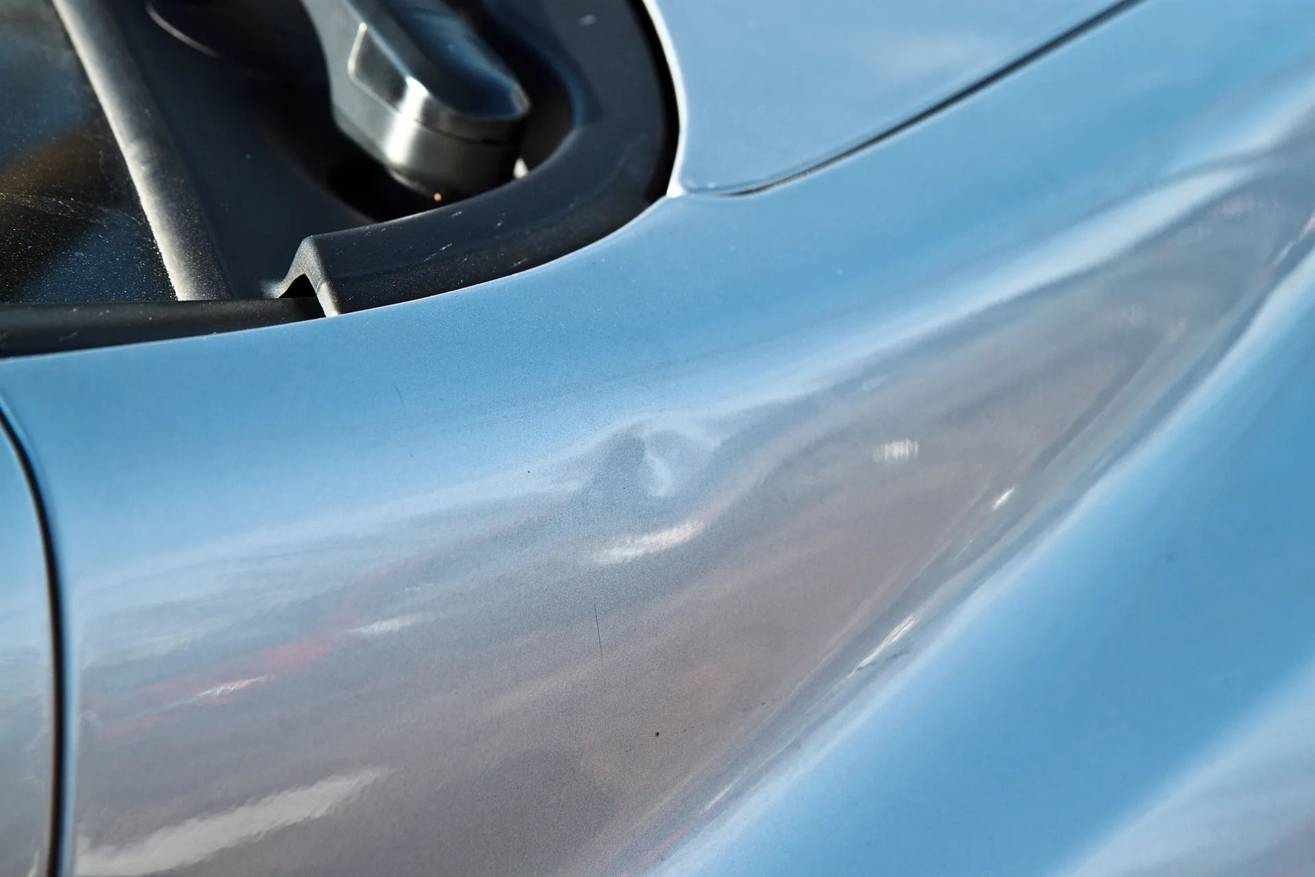 Silver car panel with a small dent near the windshield.