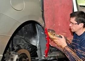 Man using a grinder on a car's red fender, sparks flying.