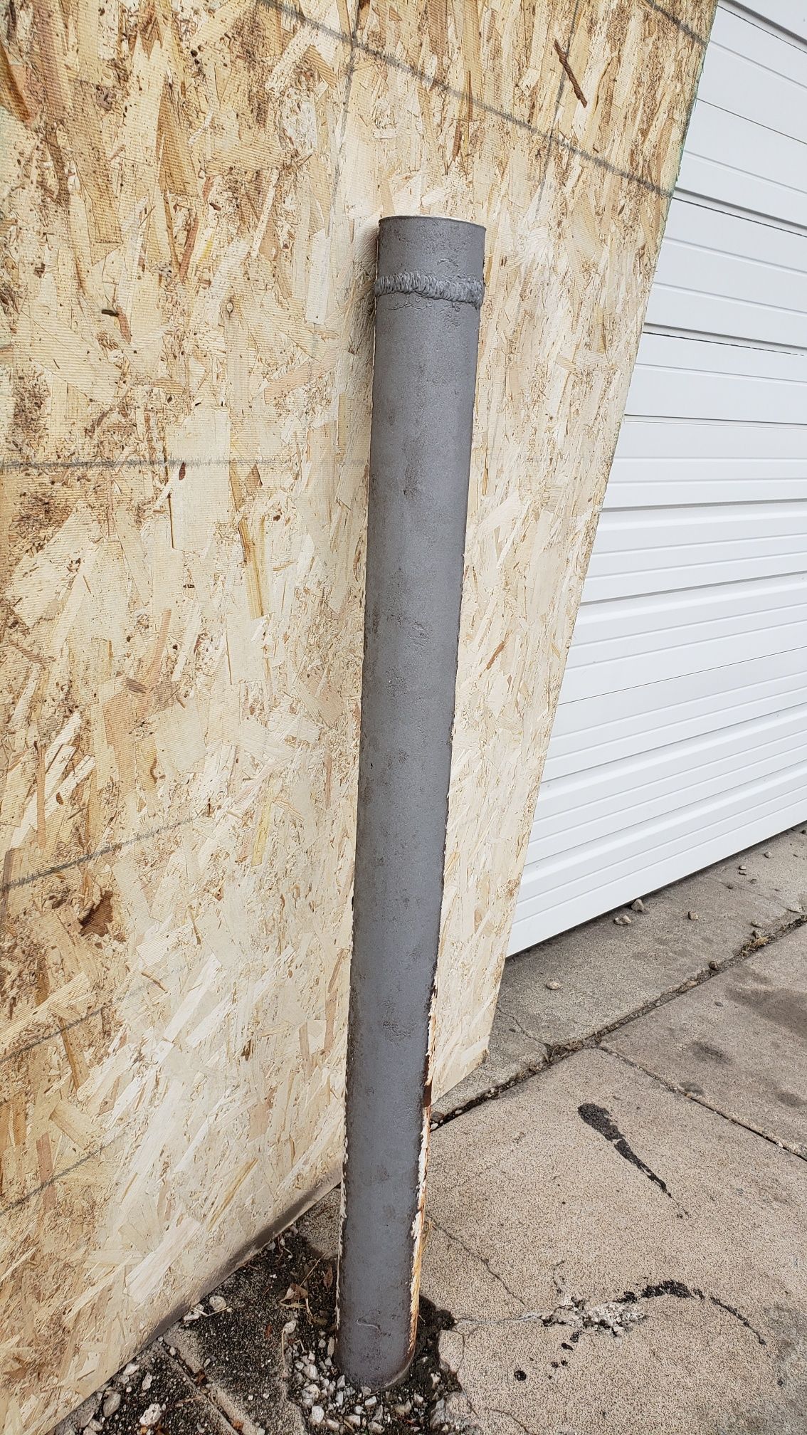 A gray pipe is leaning against a wall next to a garage door.