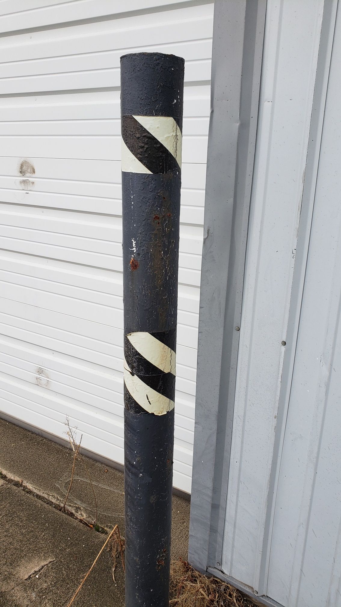 A black pole with white stripes on it is next to a garage door.