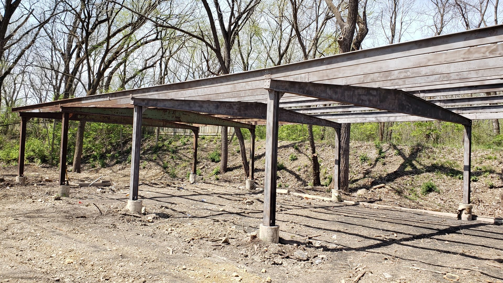 A row of metal structures in a dirt field with trees in the background.