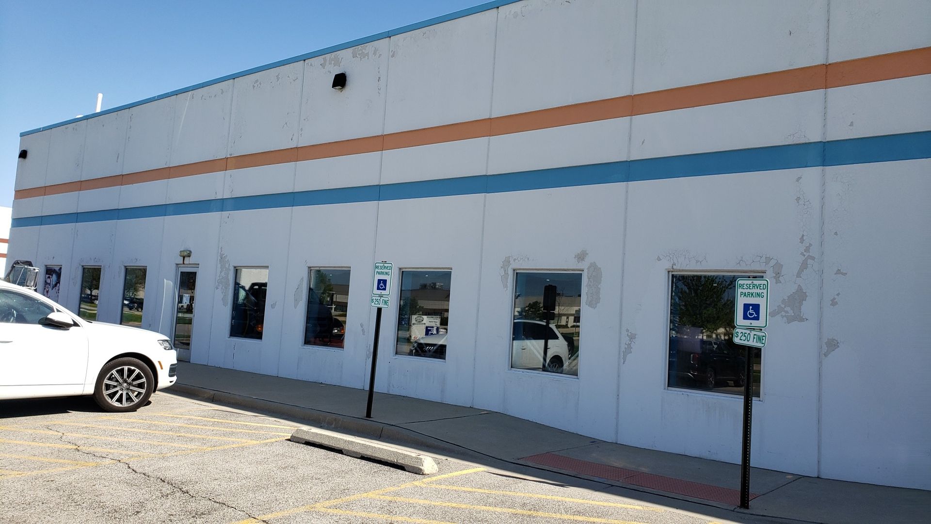 A white car is parked in front of a large white building.