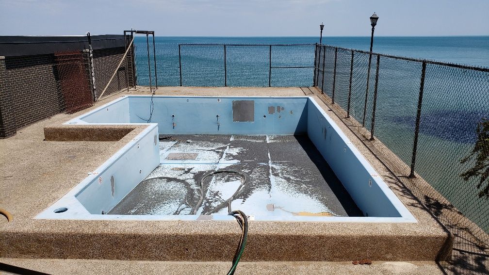 An empty swimming pool next to the ocean with a hose attached to it
