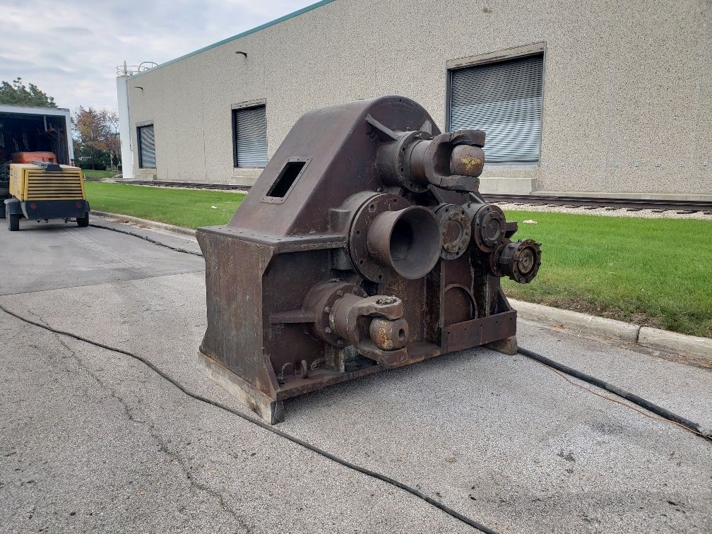A large machine is sitting on the side of the road in front of a building.