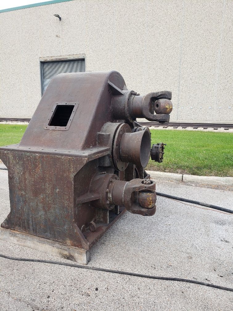 A large rusty machine is sitting on the side of the road in front of a building.