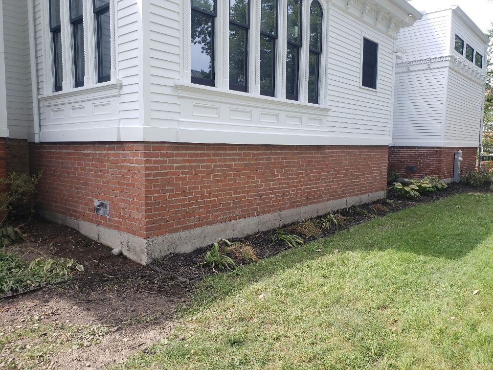 A white house with a red brick foundation is sitting on top of a lush green lawn.