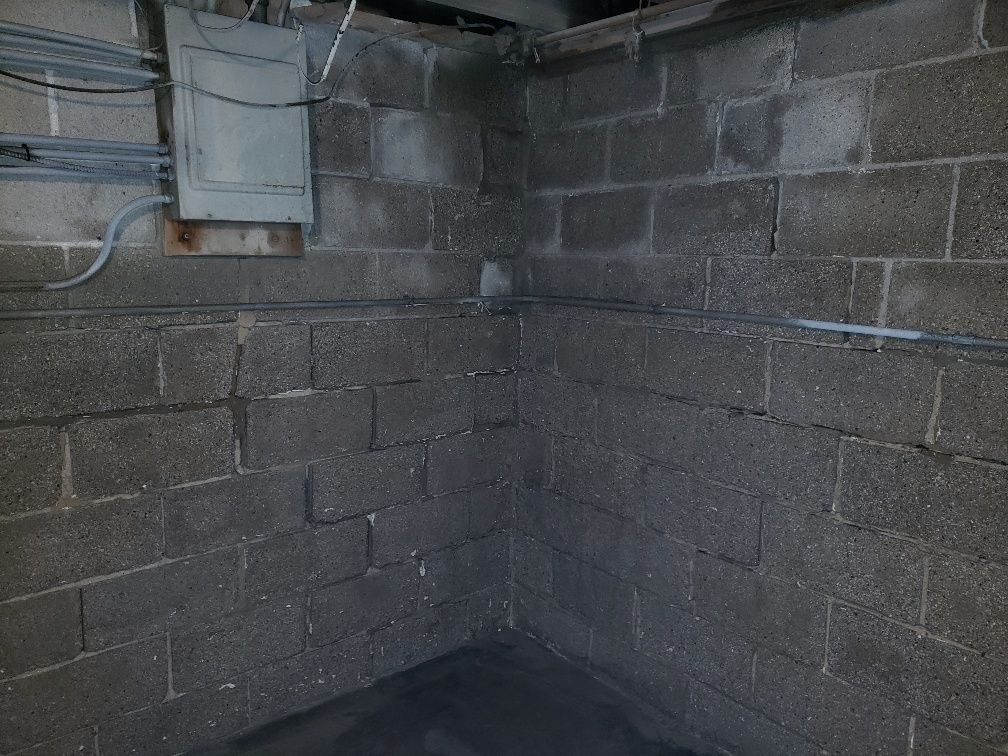 A corner of a basement with brick walls and electrical wires.