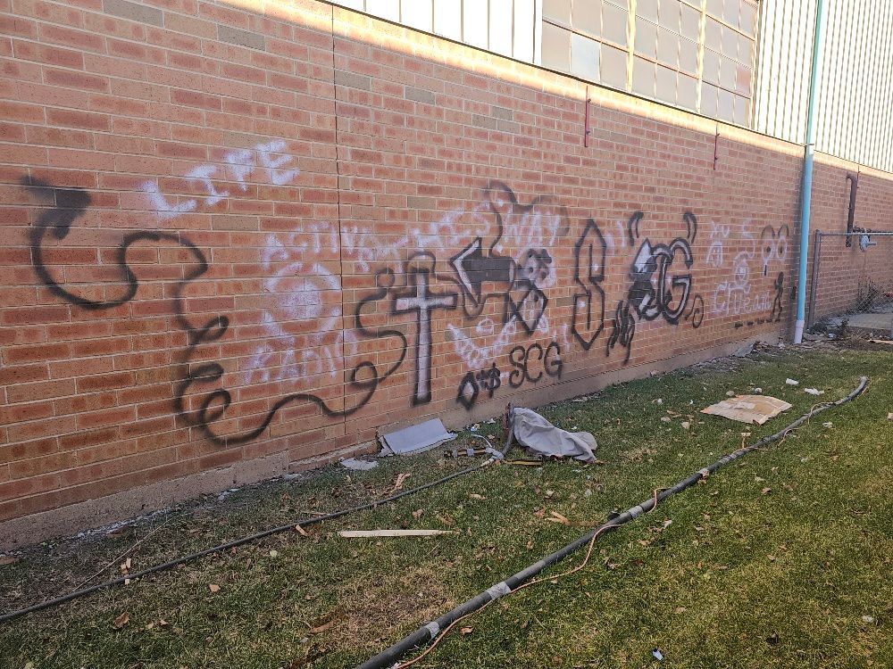 A brick wall with graffiti on it is sitting next to a grassy area.
