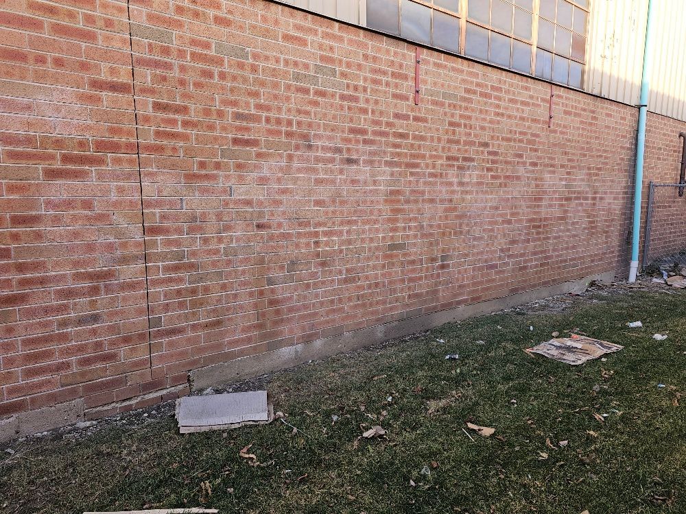 A brick wall with graffiti on it is sitting next to a grassy area.