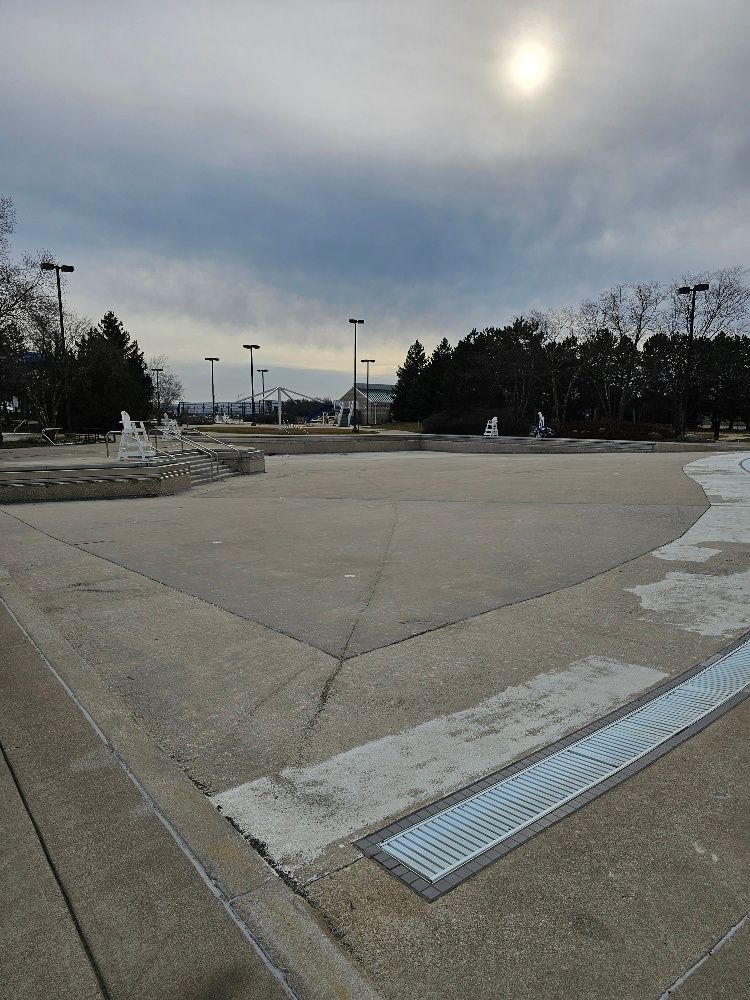 A large empty parking lot with trees in the background and the sun shining through the clouds.