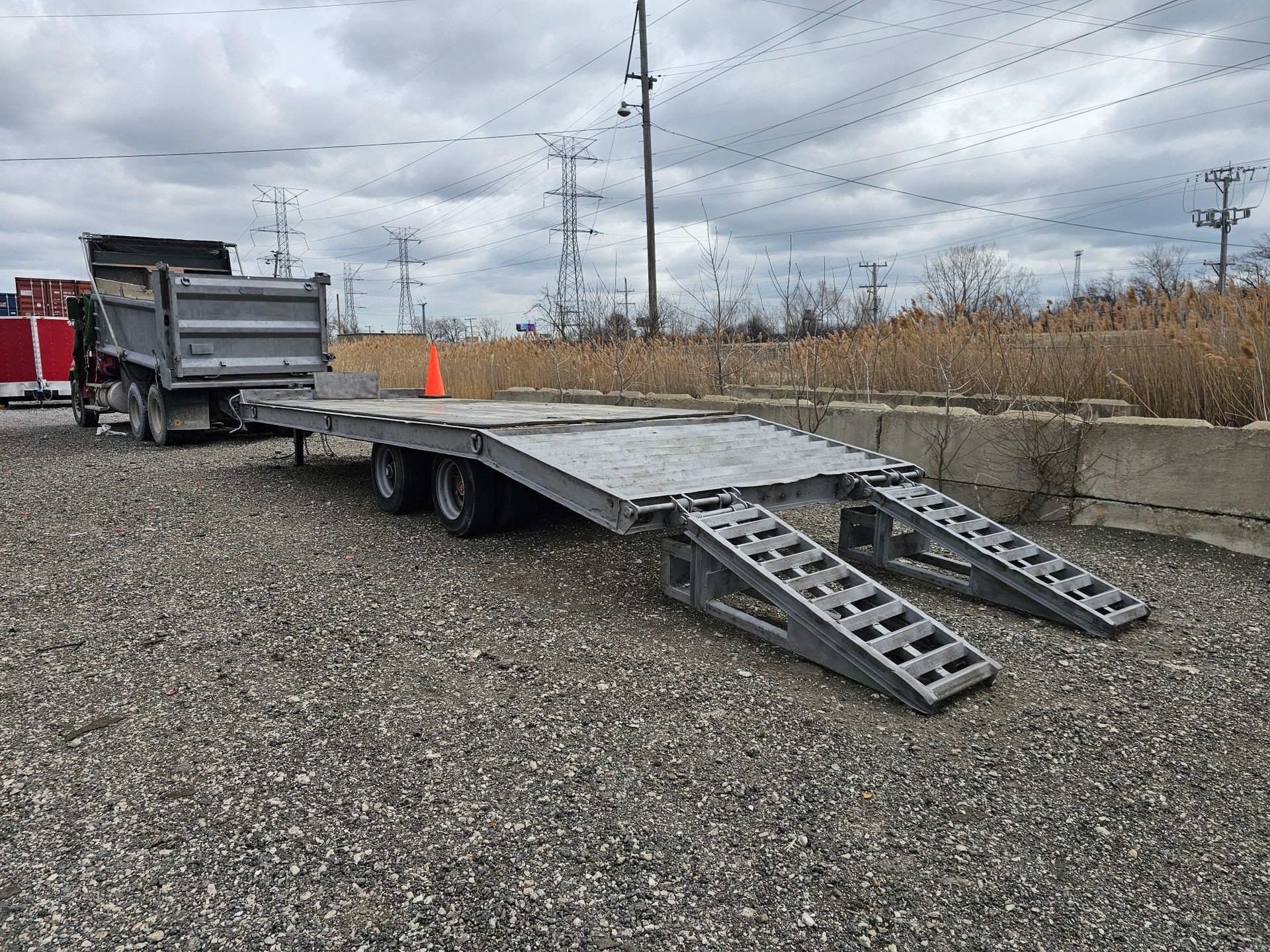 A dump truck is parked next to a flatbed trailer with ramps.