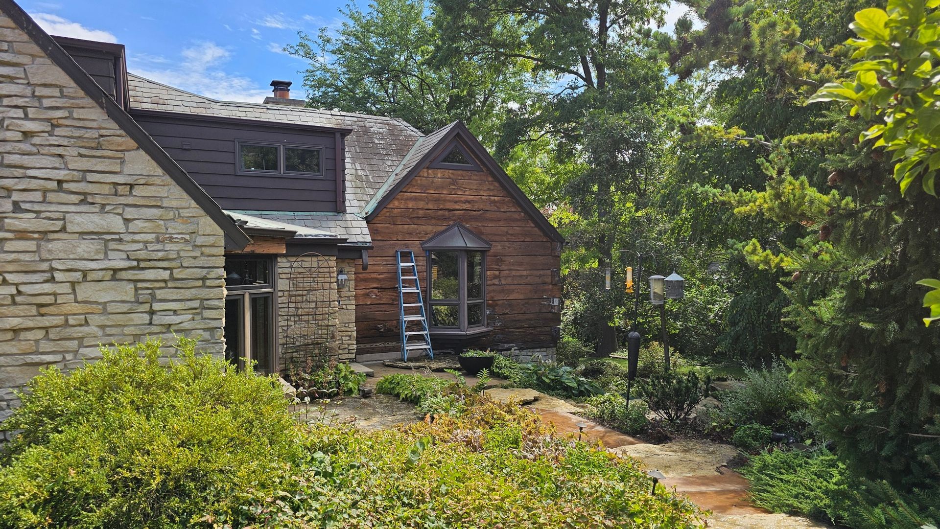 A stone house with a wooden roof is surrounded by trees and bushes.