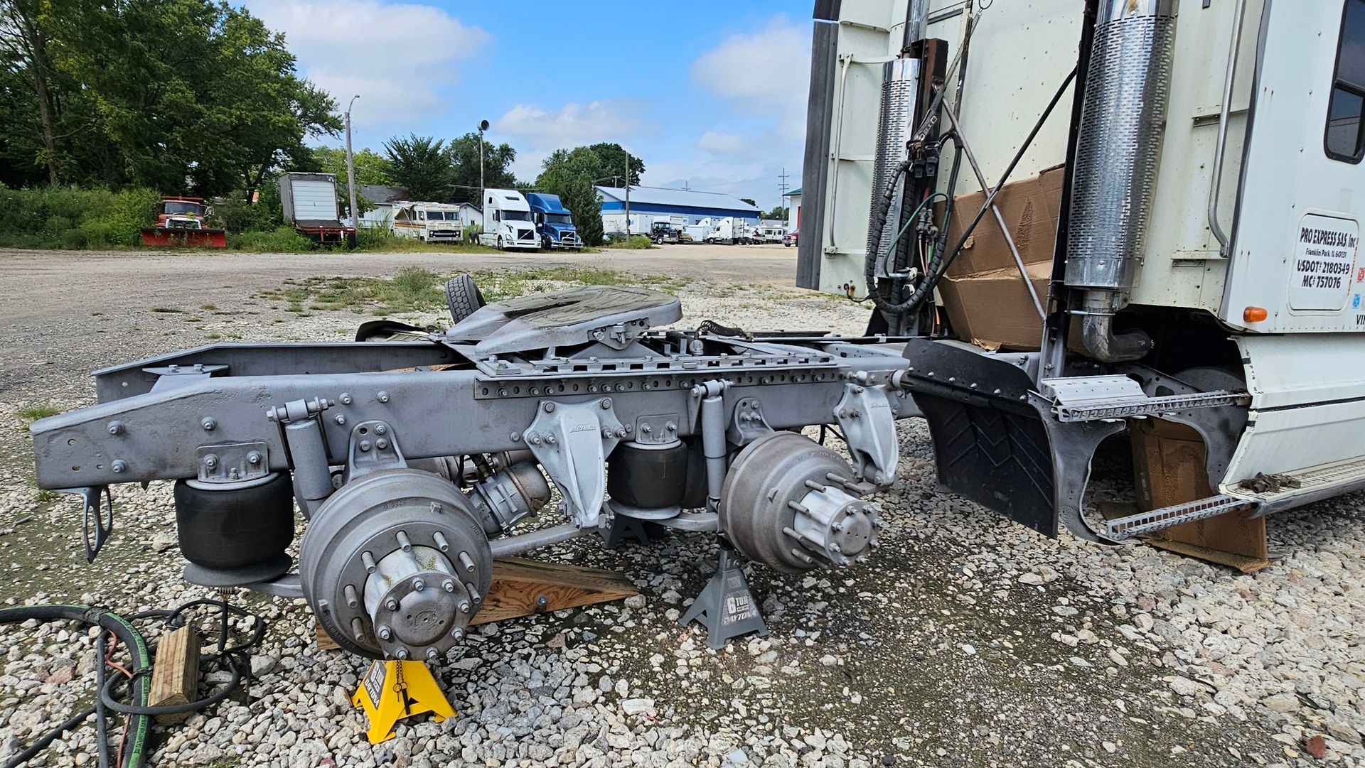 A semi truck is sitting on the ground in a gravel lot.