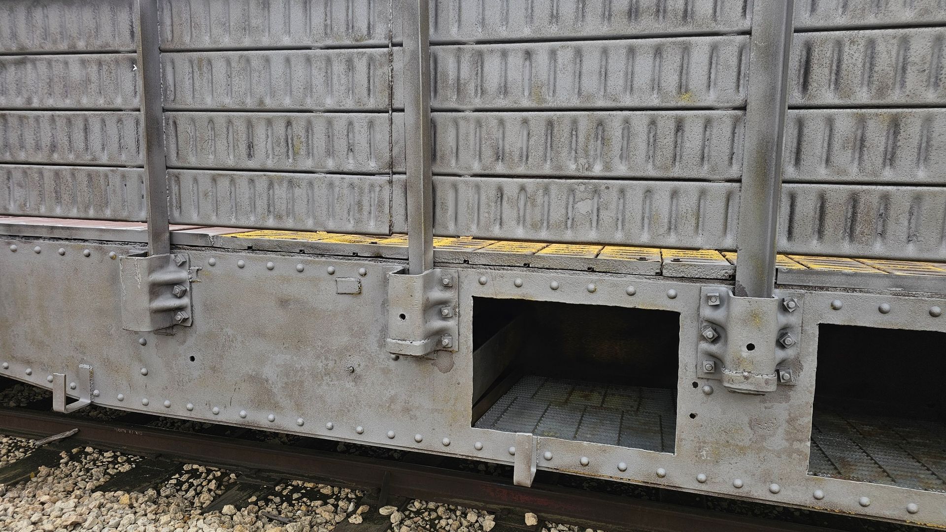 A train car is sitting on the tracks with a brick wall behind it.