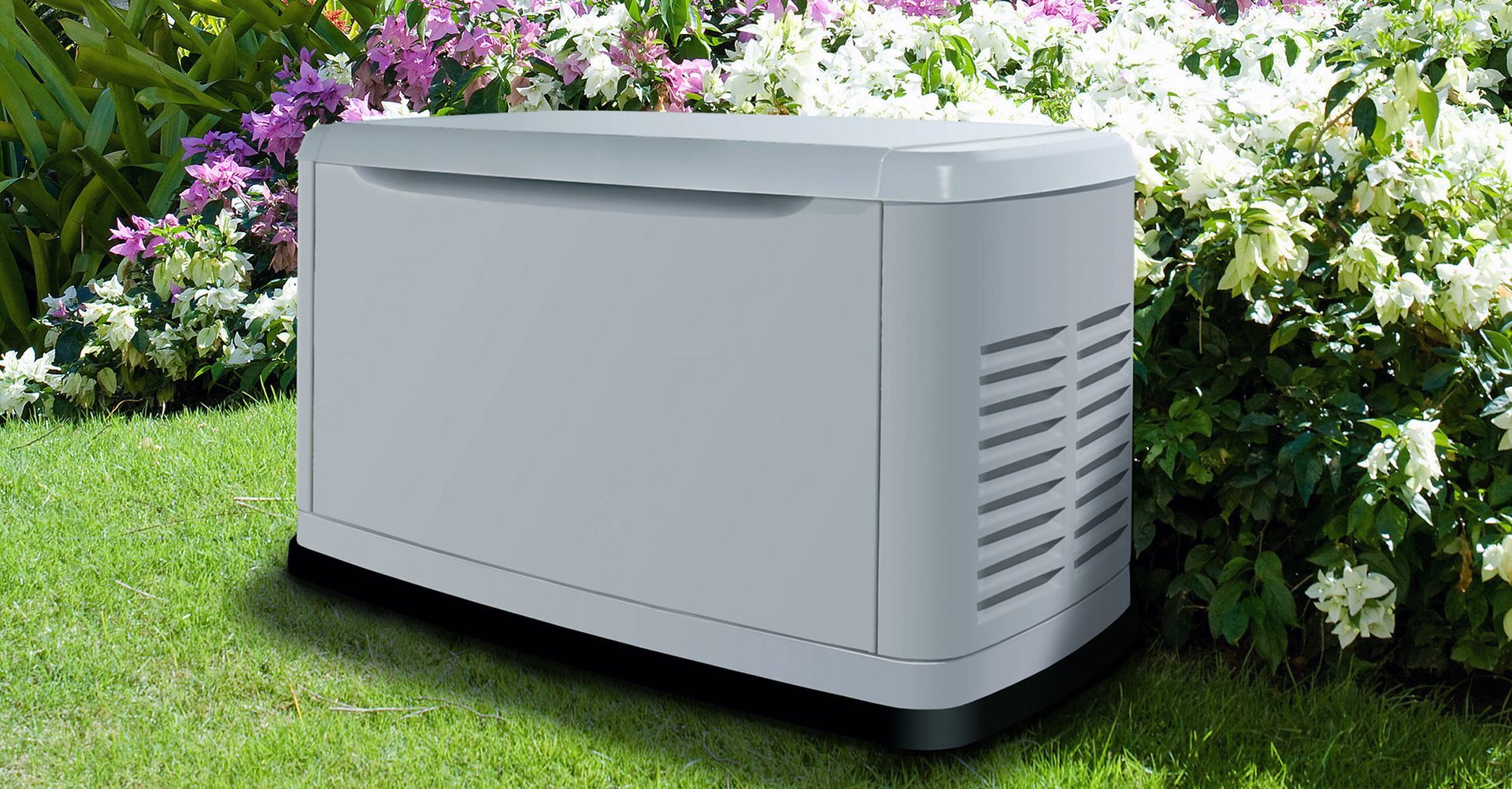 A white generator is sitting in the grass next to flowers.