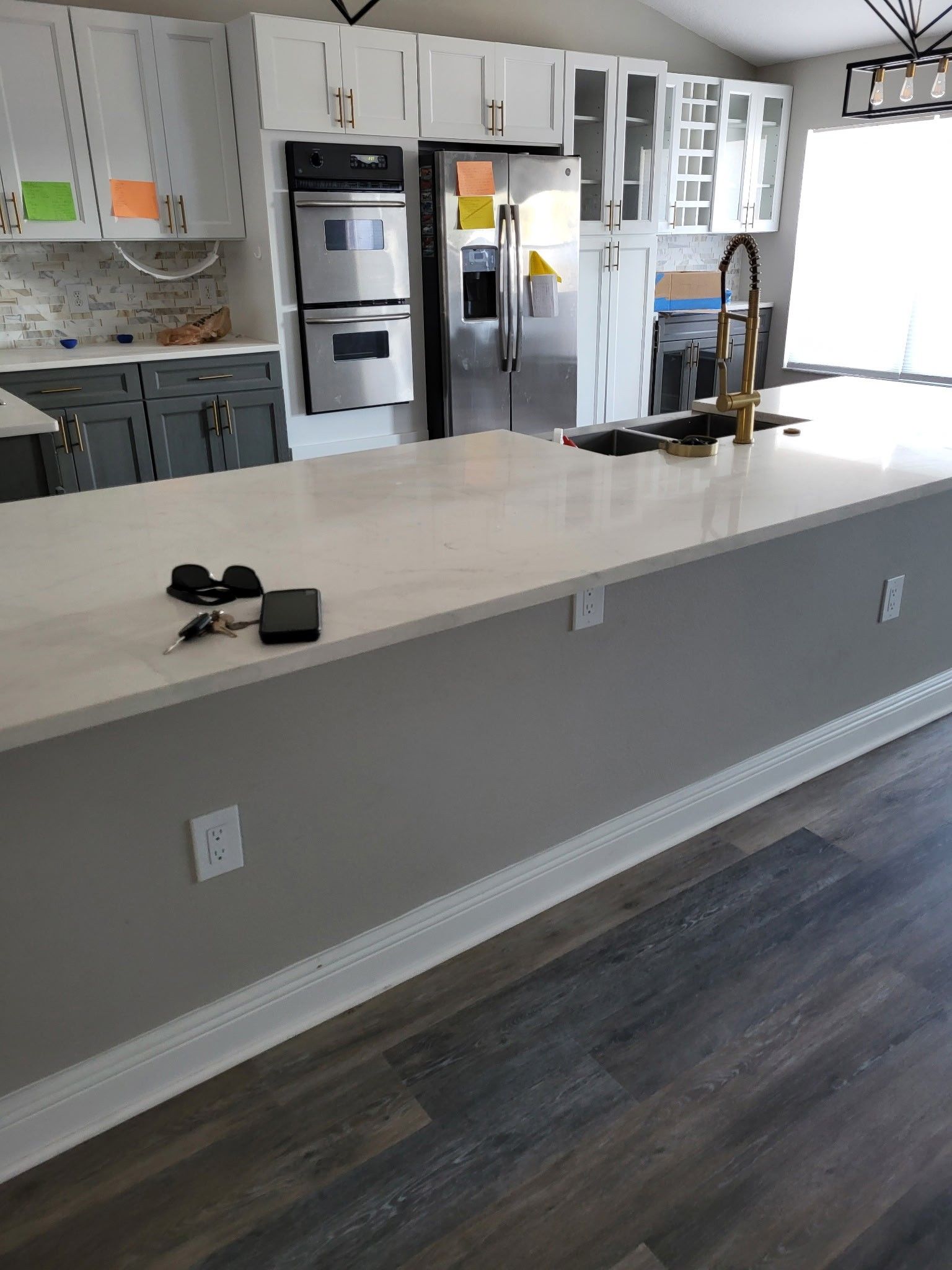 Kitchen island with white countertop, gray cabinets, and gold faucet. Black appliances and dark wood flooring.