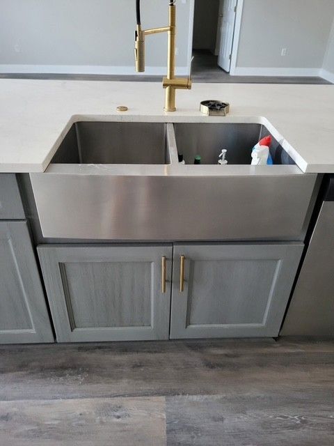 Stainless steel farmhouse sink with gold faucet in a gray kitchen island.