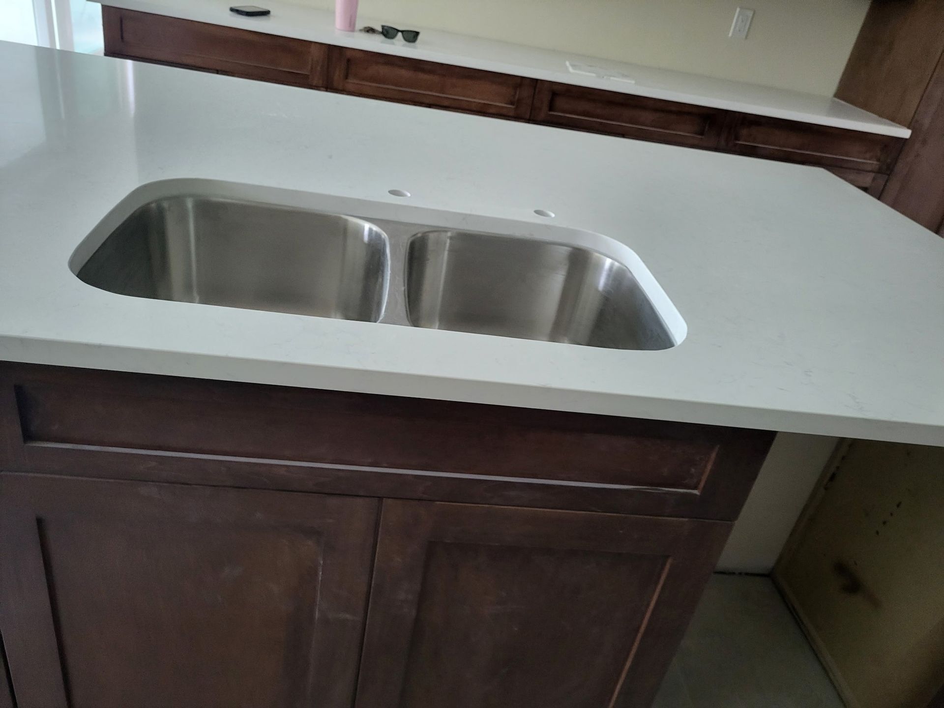 Kitchen with a stainless steel double sink in a light-colored countertop, dark brown cabinets below.