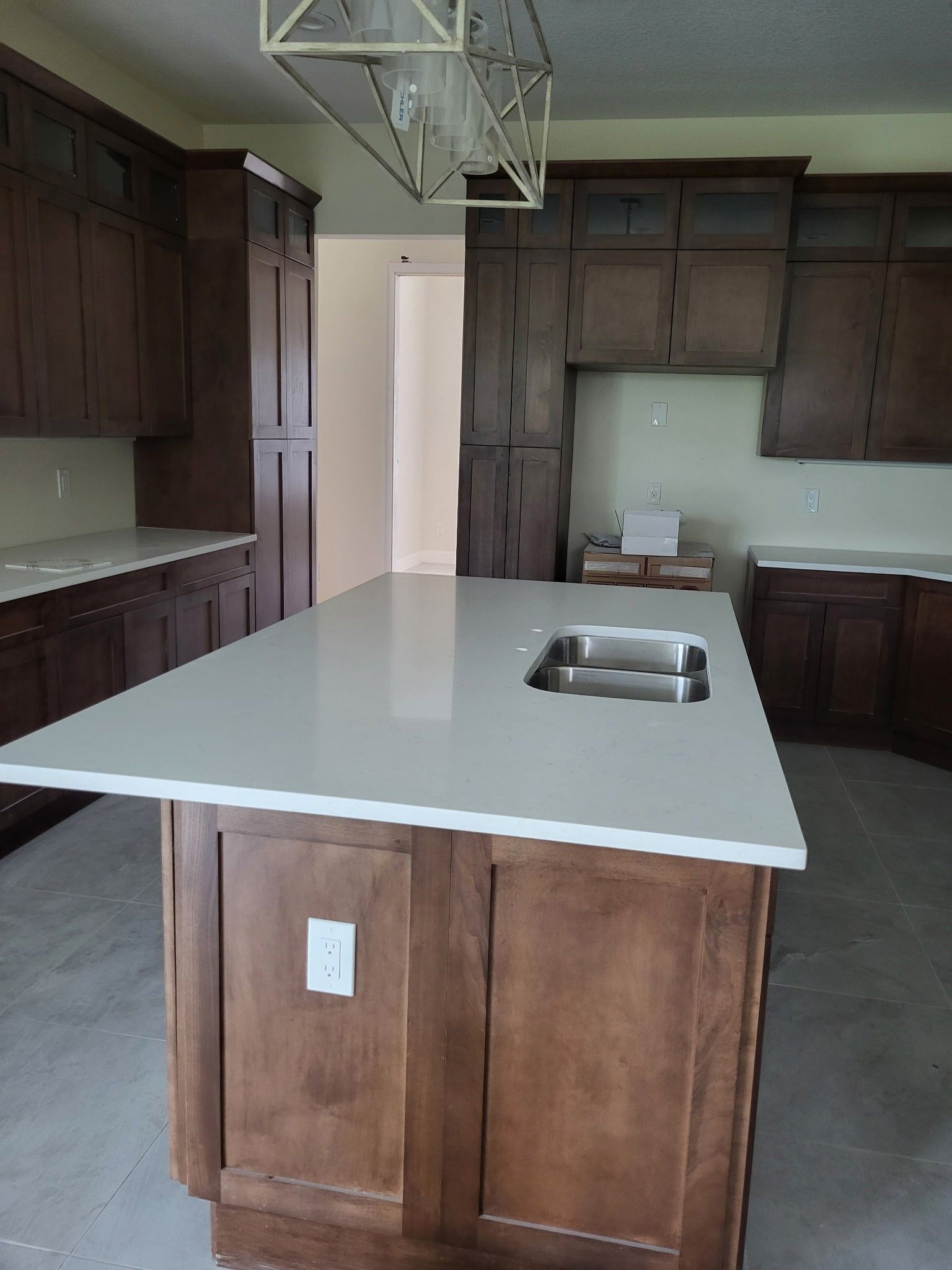 Kitchen with brown cabinets, light countertops, island with sink, and a light fixture.