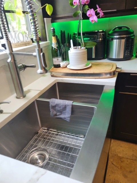 Stainless steel kitchen sink with a faucet and a drying rack. There are countertops, and appliances are in the background.