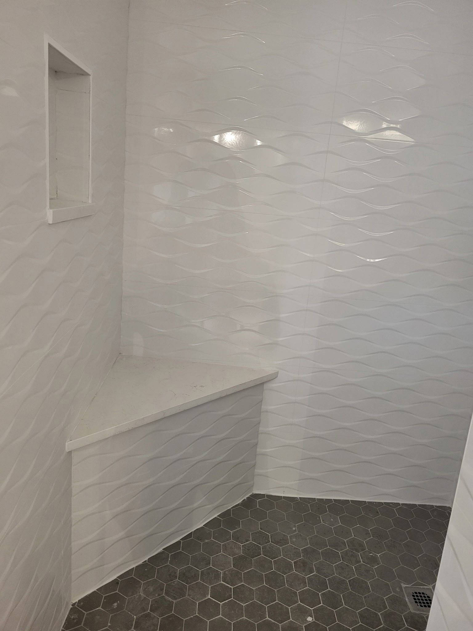 White-tiled shower with built-in bench and recessed shelf, dark hexagon floor tiles.