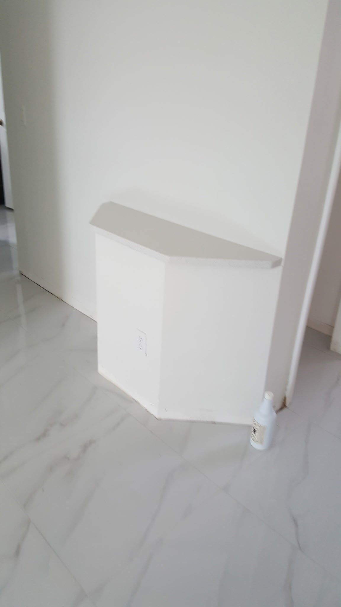 White corner cabinet on a tiled floor, near a white wall and a light-colored doorframe.