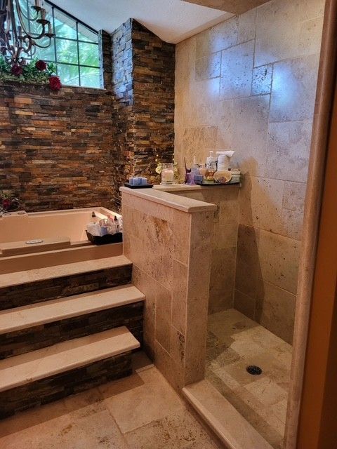 Bathroom with step-up bathtub, stone walls, shower, and window.