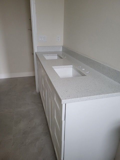 white bathroom vanity with two sinks, gray countertop, white cabinets, against a light-colored wall