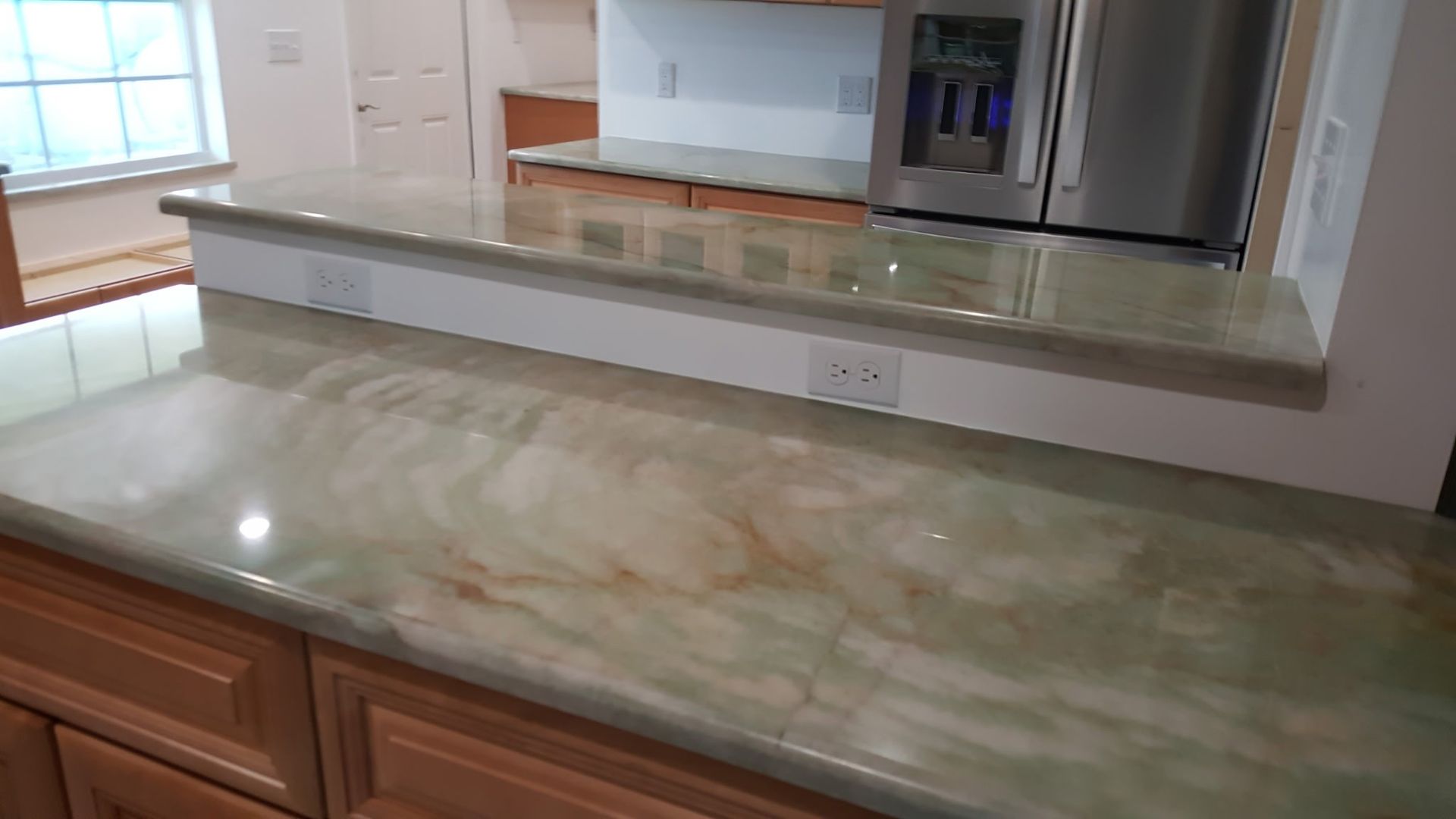 green and brown marble countertop on wooden cabinets in a kitchen, with a stainless steel refrigerator