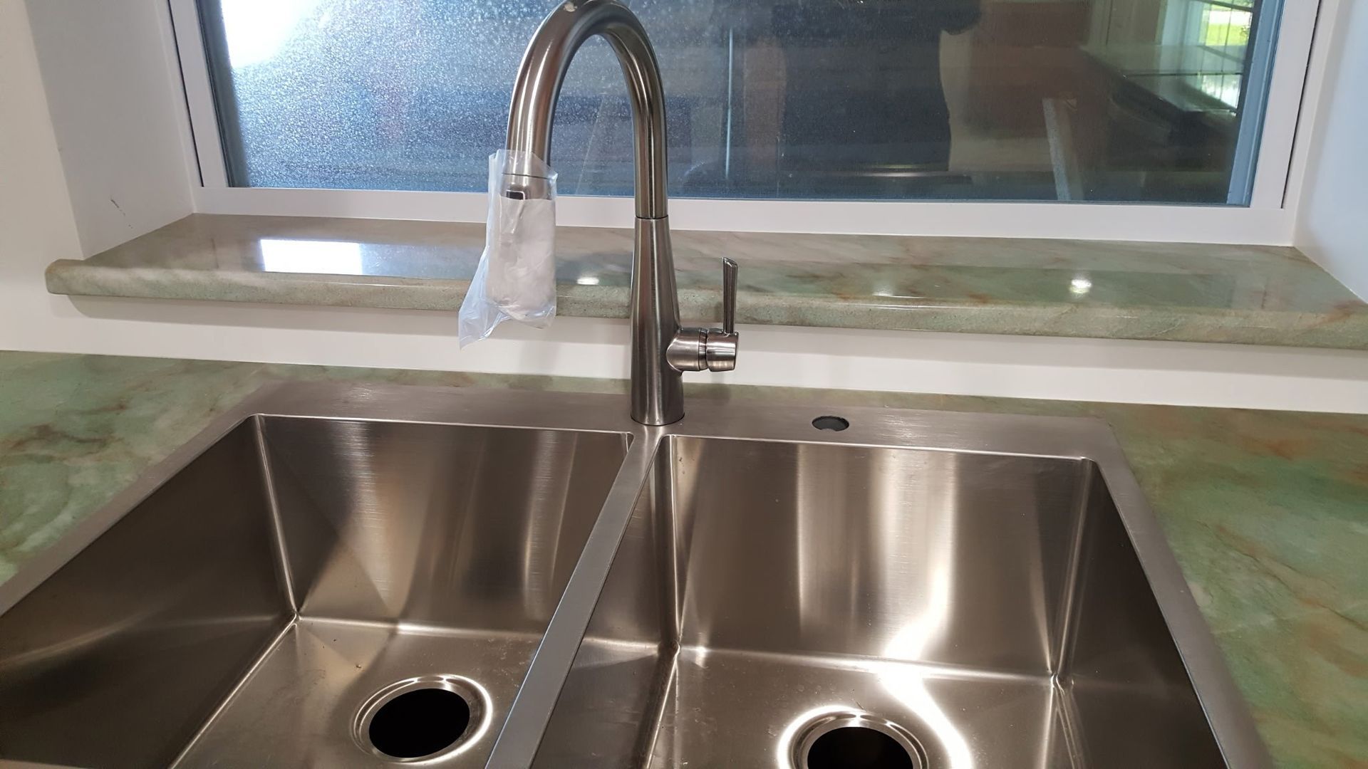 stainless steel double sink with faucet, set against a window with a green countertop