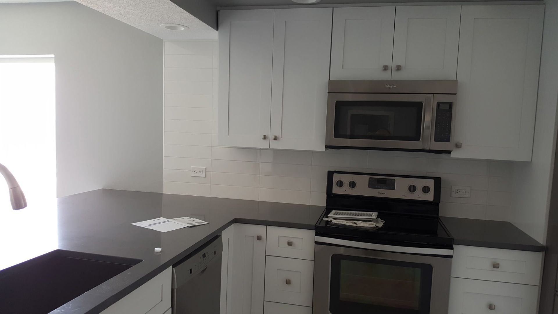 L-shaped kitchen with white cabinets, gray countertops, stainless steel appliances, and a tiled backsplash