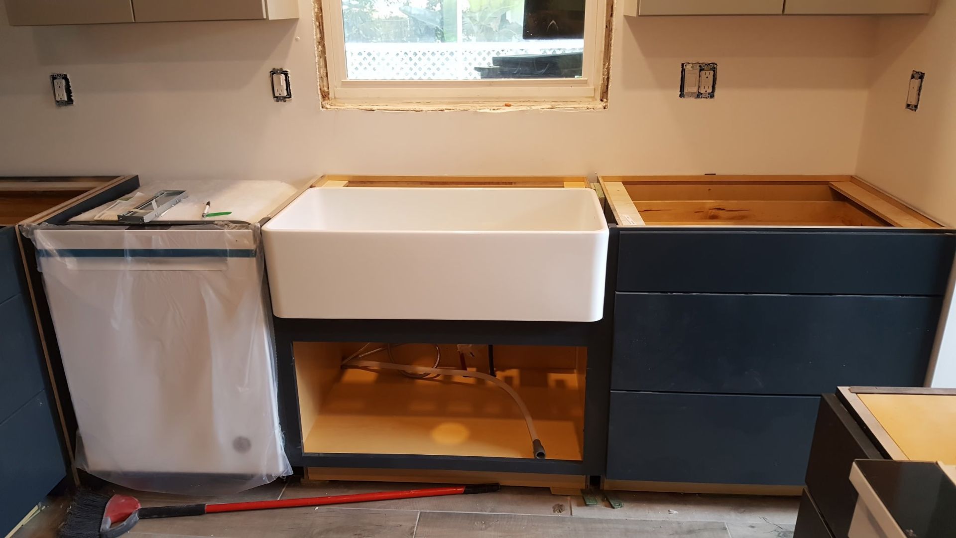 kitchen under construction with a white farmhouse sink installed and dark blue cabinets