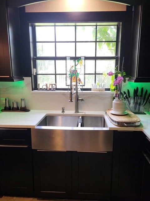 stainless steel kitchen sink under a window, black cabinets, white countertop