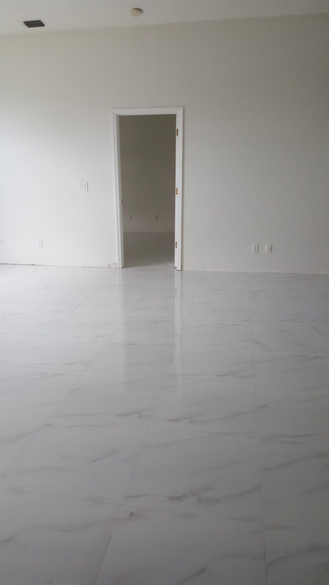 empty room with white tile floor and walls, a door frame, and minimal fixtures
