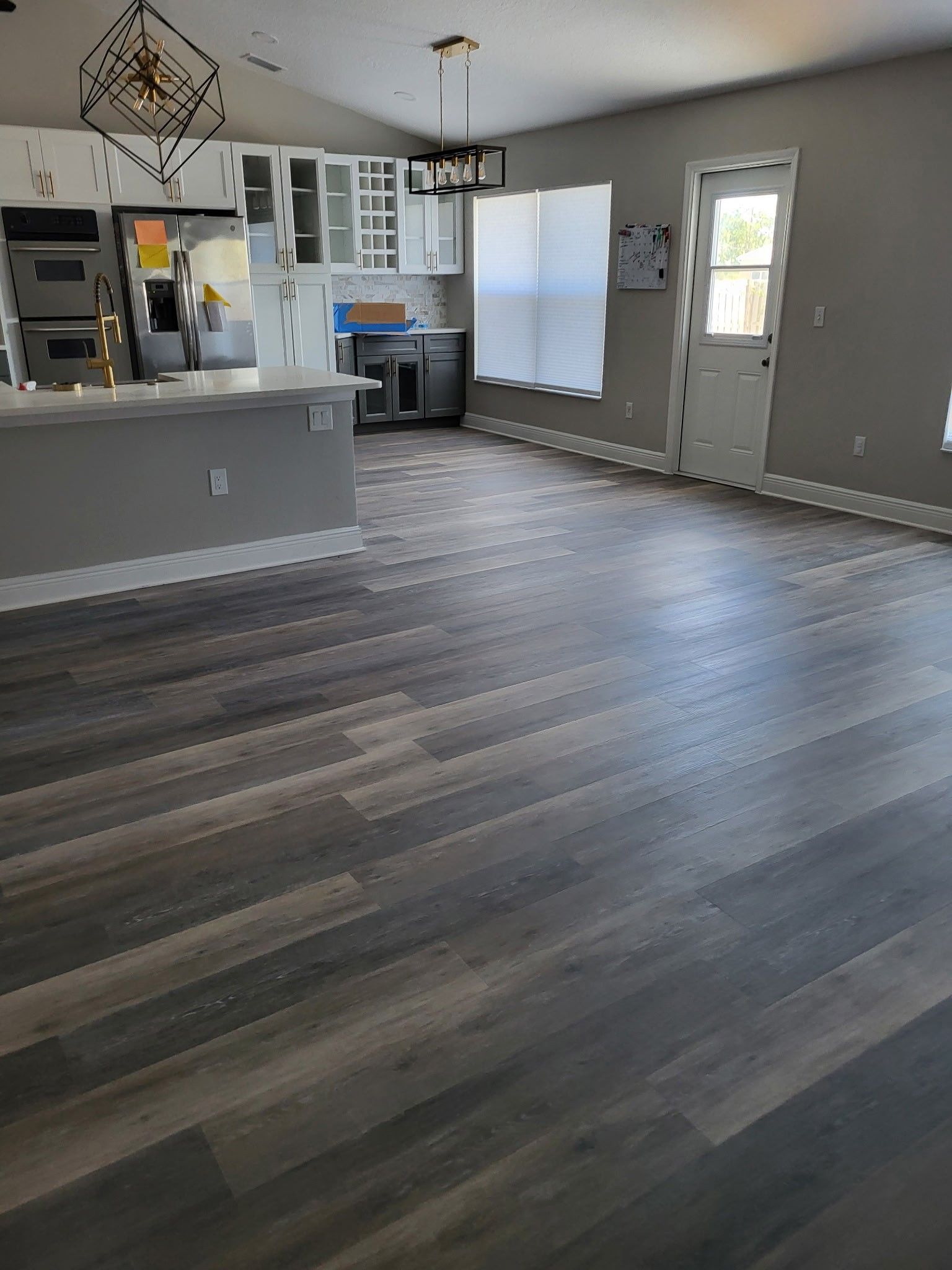 gray laminate flooring in an open-concept kitchen and living area with white cabinets and a door