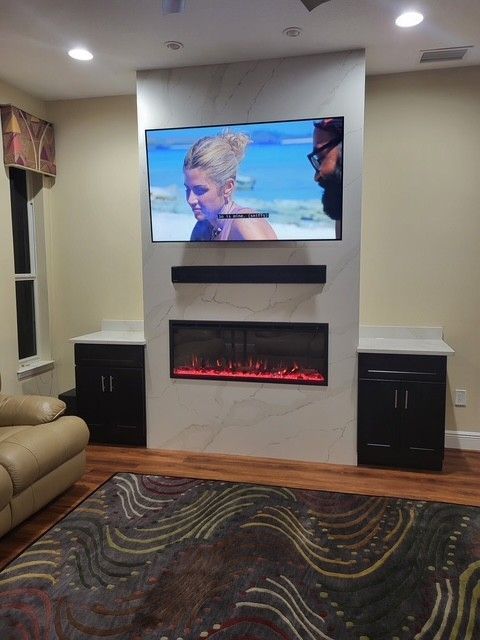 a living room with a TV, soundbar, and fireplace built into a marble accent wall, flanked by dark cabinets